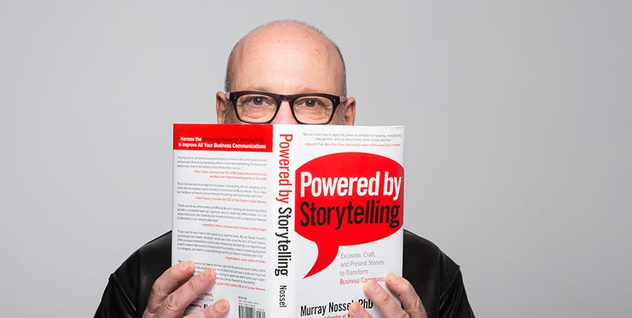 author murray nossel pictured with a copy of his book Powered by Storytelling