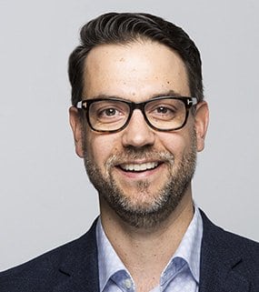 a man in a suit and glasses smiling.