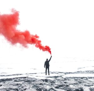 selective color photography of person holding orange gas smoke standing on snow