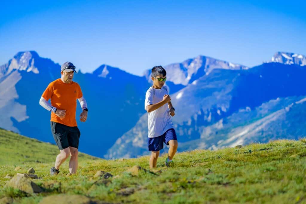 man and boy running on green grass field at daytime