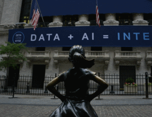 A bronze statue of a girl stands facing a building displaying a large banner that reads "DATA + AI =" with American flags above.